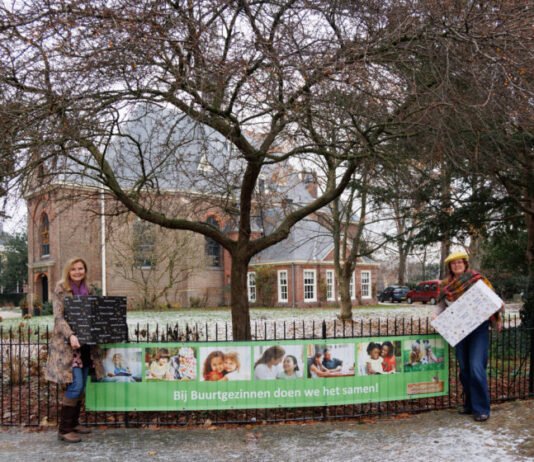 Buurtgezinnen Bloemendaal in kerstactie voor gezinnen (van links naar recht) Paulien de Jong en Anne-Marie Scheeres van Buurtgezinnen Bloemendaal bij de banner aan het hek van de Dorpskerk van Bloemendaal.
